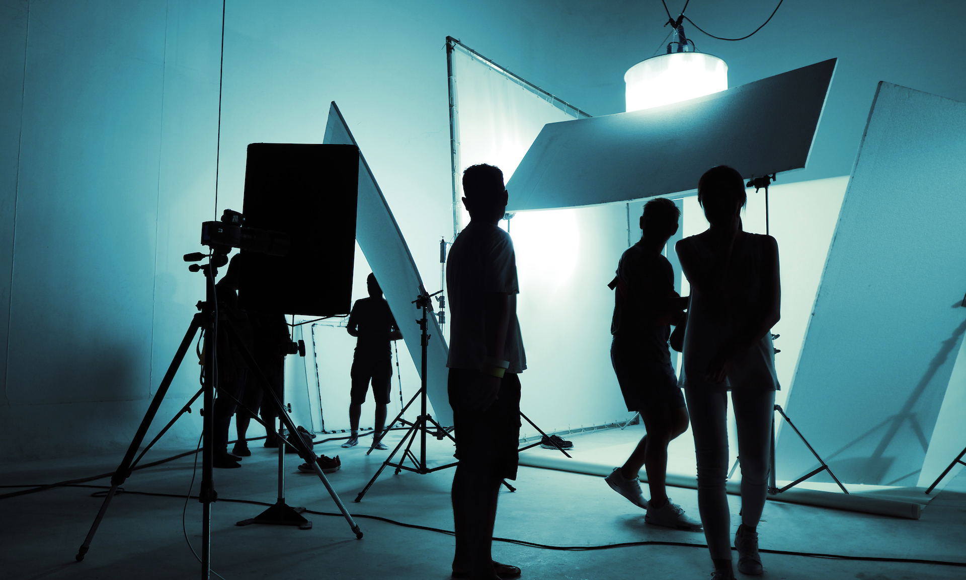 A photo-shoot crew in silhouette around lights and reflectors in a studio