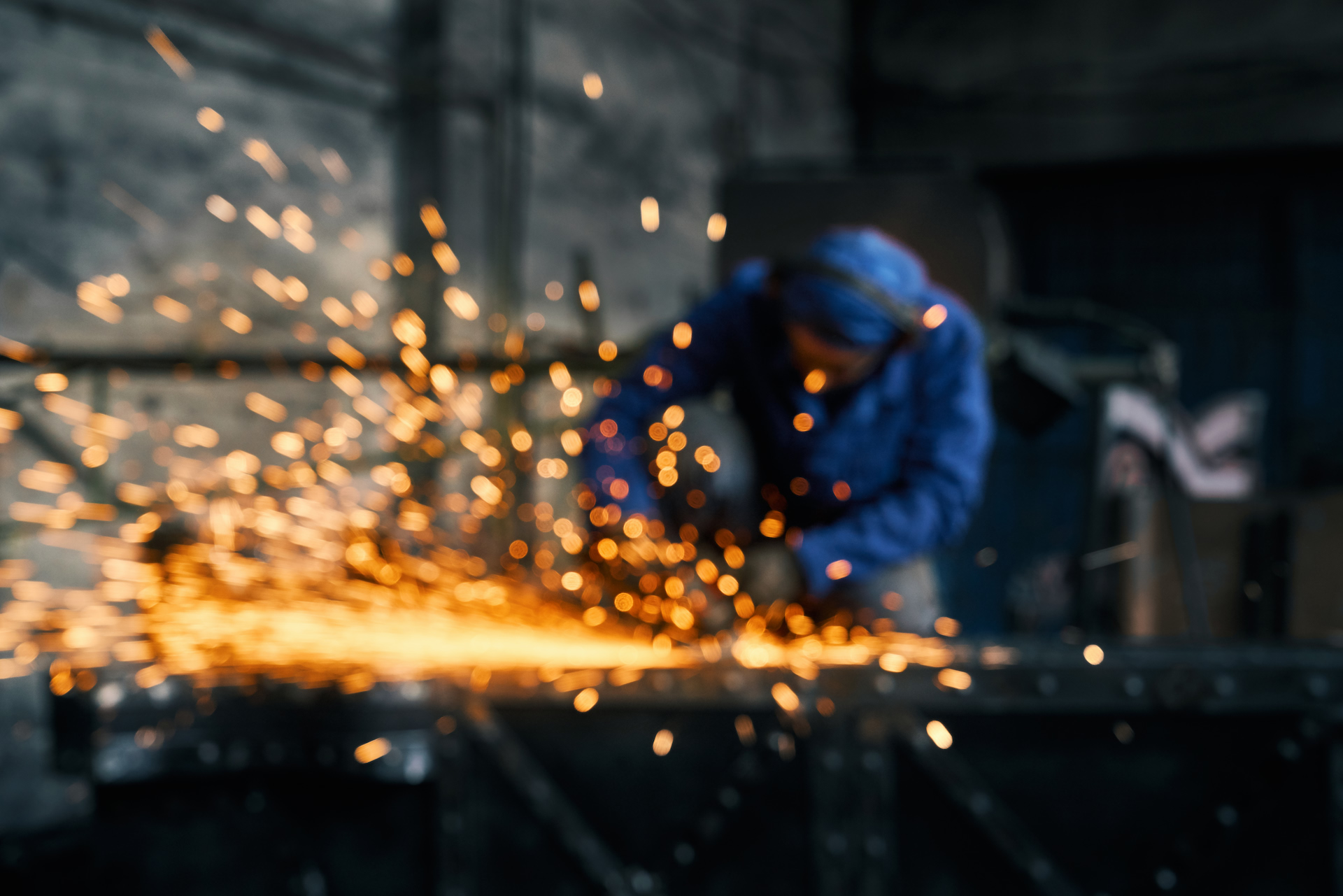A metalworker cutting steel, sparks flying across the frame