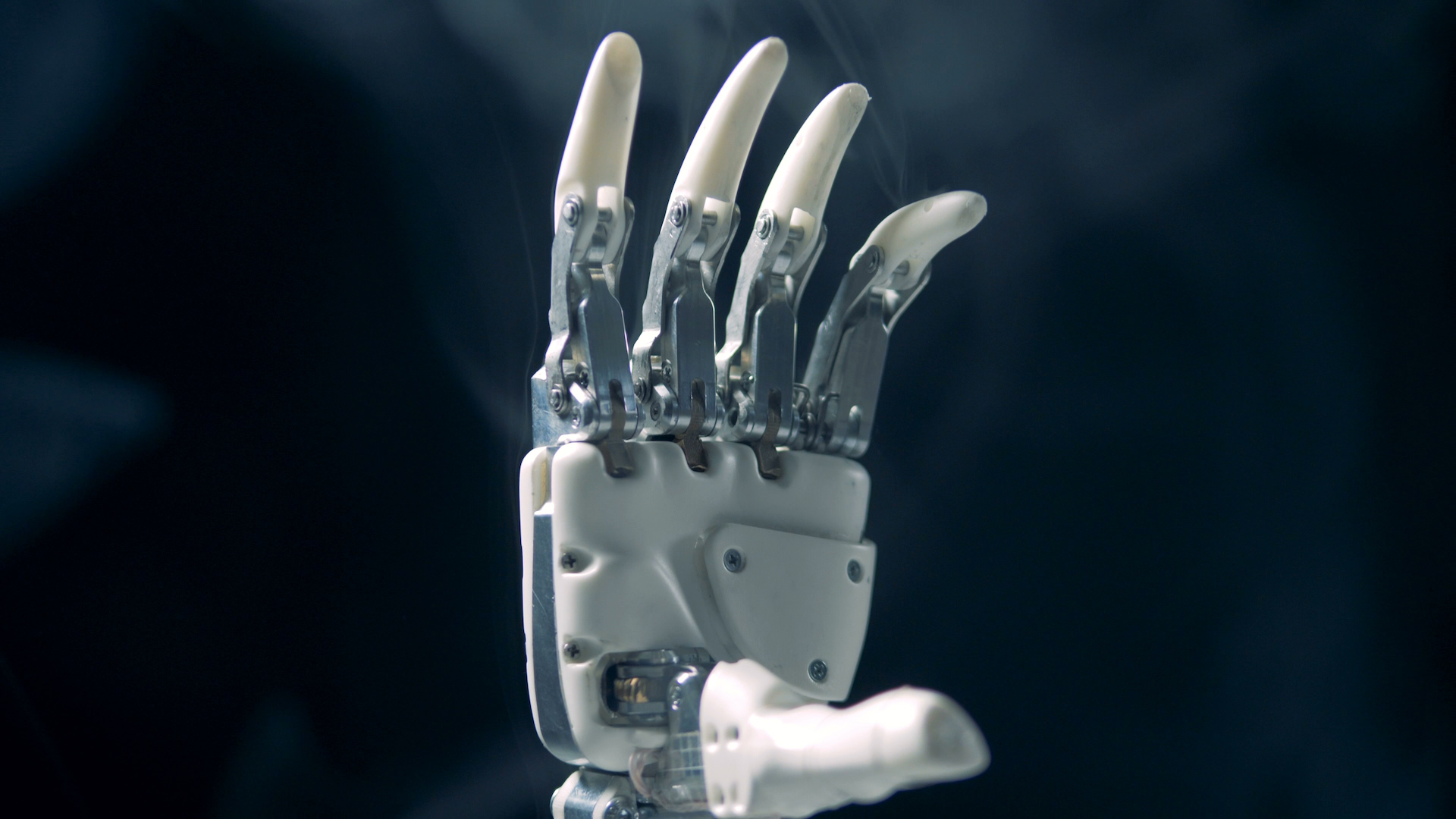 A white robotic hand, its fingers raised, in drifting smoke against dark blue