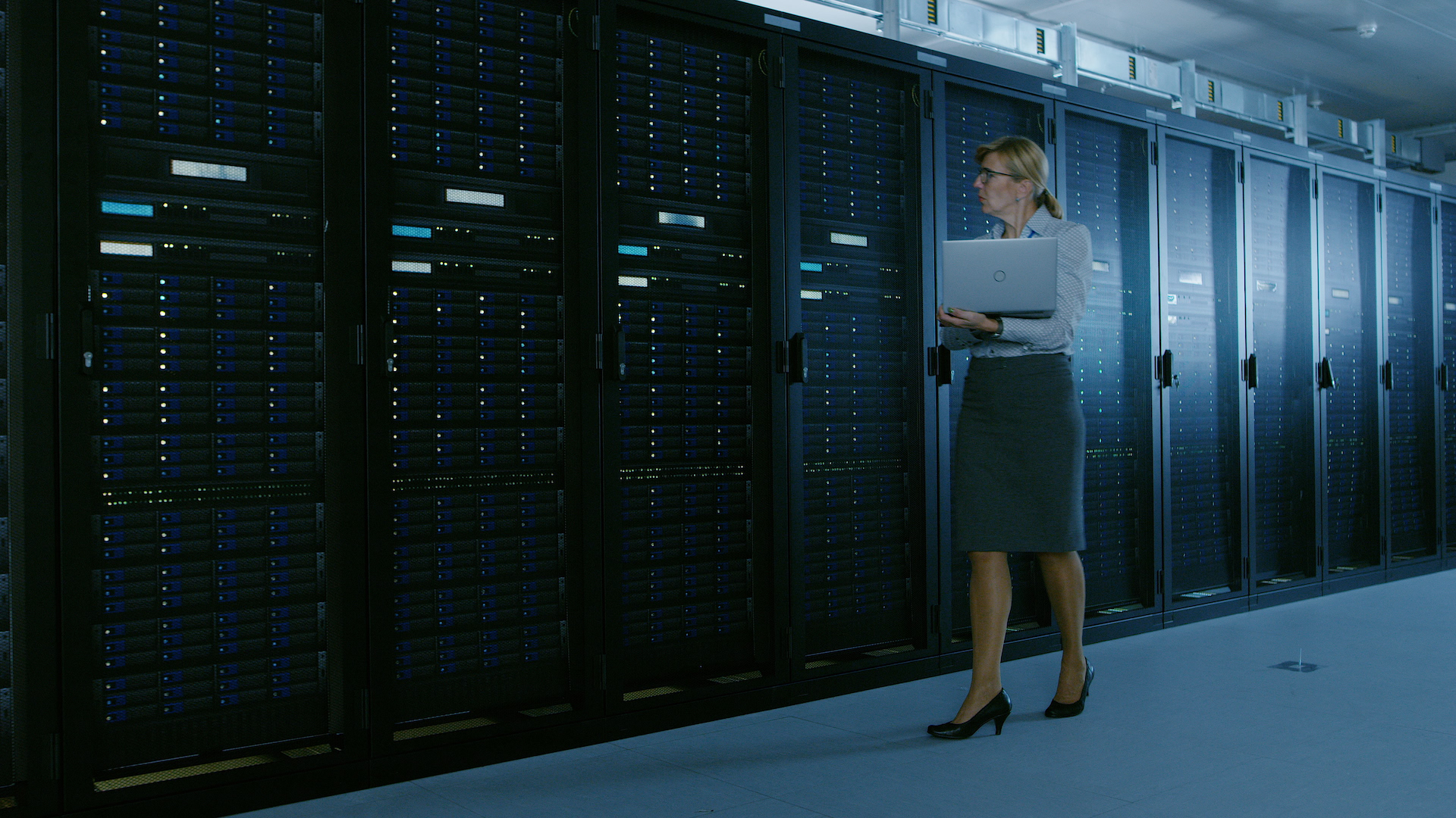 An engineer with a laptop walking along a row of server racks in a data centre