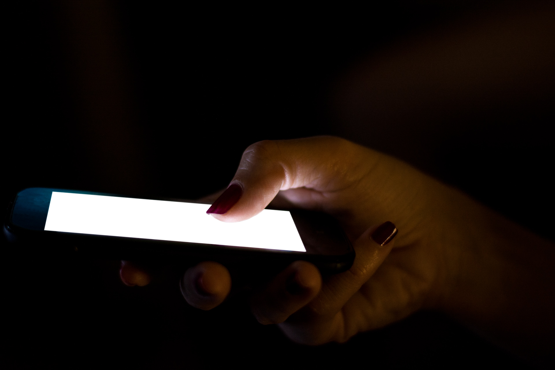 A hand holding a lit smartphone in the dark