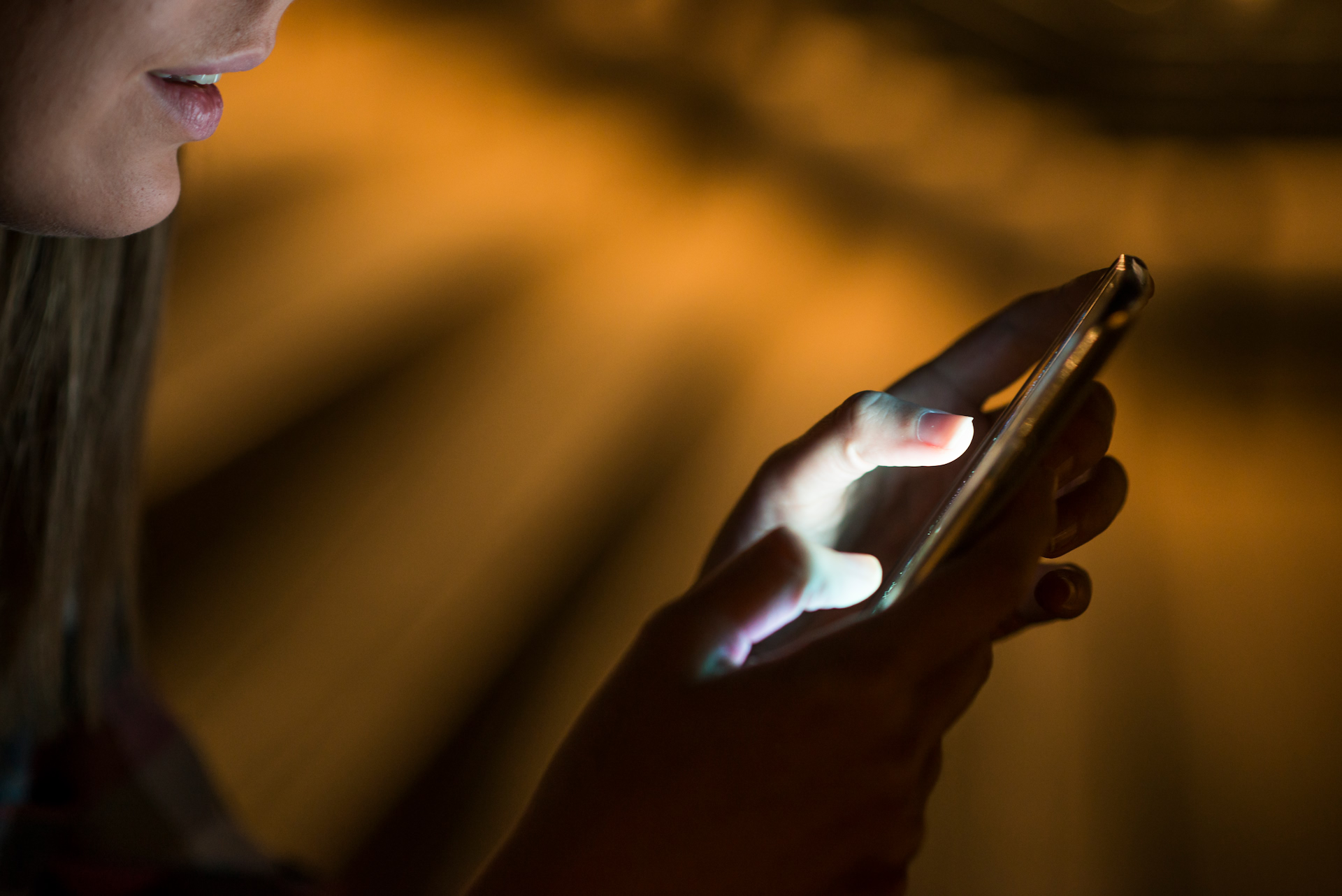 A woman using her phone, warm city lights behind