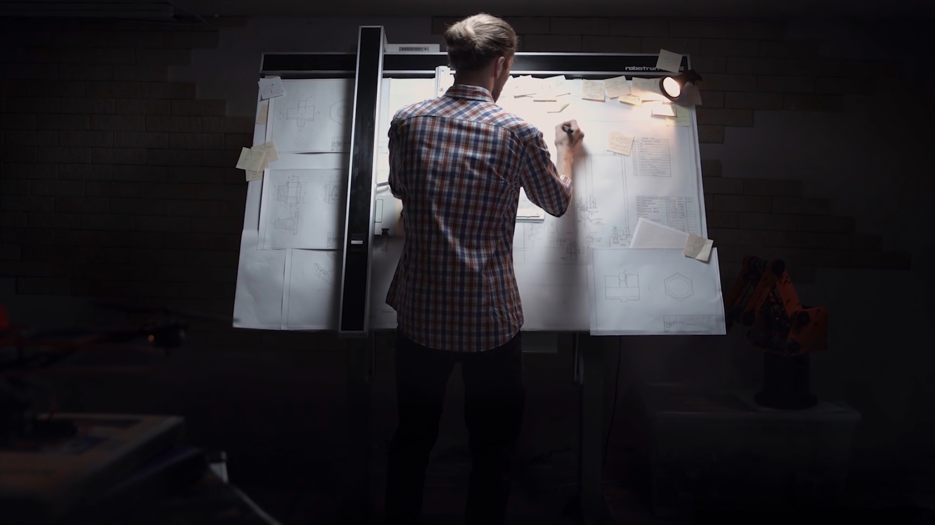 A man drawing a diagram on a large lit board in a dark room