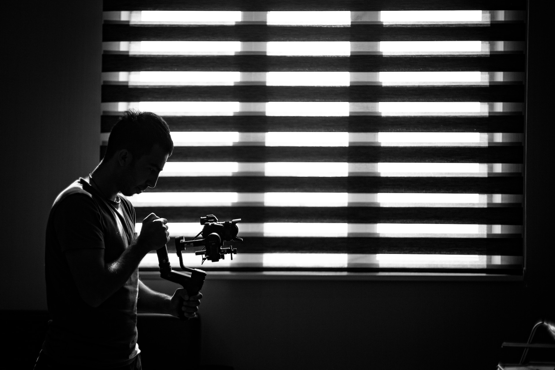 A photographer checking a camera in a dark room lit through window blinds