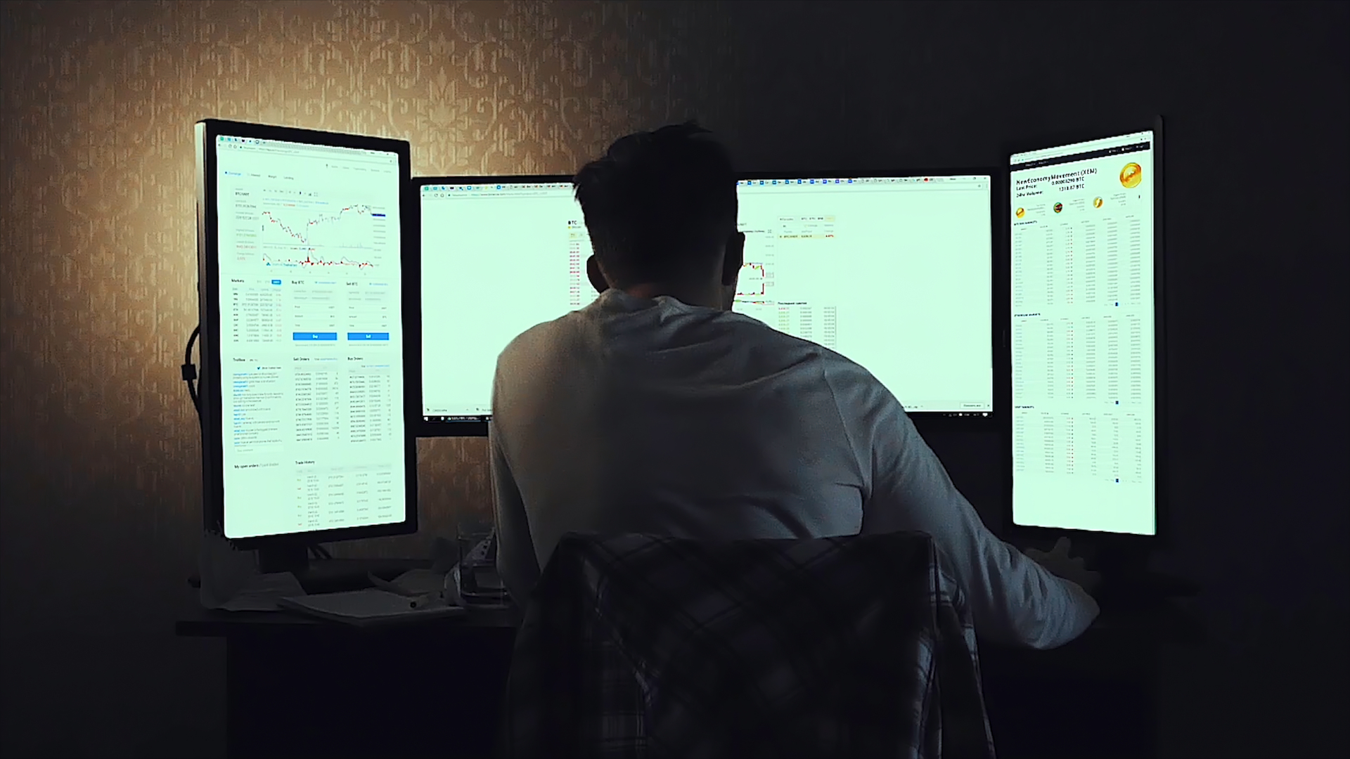 A programmer from behind, working across three monitors in a dark room